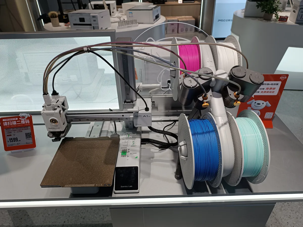 Bambu Lab A1 mini beside an optional AMS lite with four filament spools in a showroom
